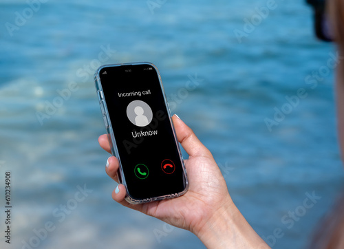 Incoming call with unknown caller, malicious phone calls concept. Unknown number displayed showing on smart mobile phone in woman hand on leave day at the beach. Spam and robocalls, scam call alert. photo