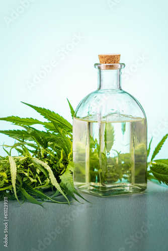 Hemp medical oil in glass bottle and fresh green cannabis leaves.