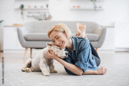 Foto Pretty smiling woman in casual wear snuggling to cute pet's head while testing comfort of wooden floor with carpet on it