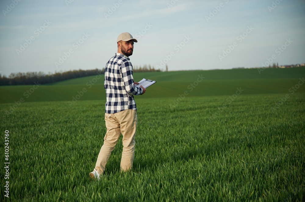 Walking, holding notepad. Handsome young man is on agricultural field Walking, holding notepad. Handsome young man is on agricultural field