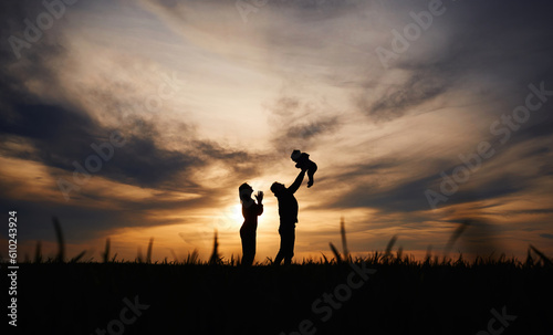 Holding little baby in hands. Silhouettes of father and mother that are outdoors against sunset dramatic sky in the field © standret