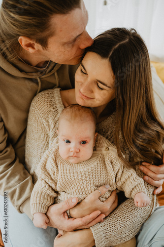 Young mother and father with their little daughter hugging and kissing on the bed.