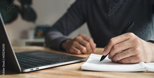 left handed man writes in a notebook on the table with laptop computer, Businessman.