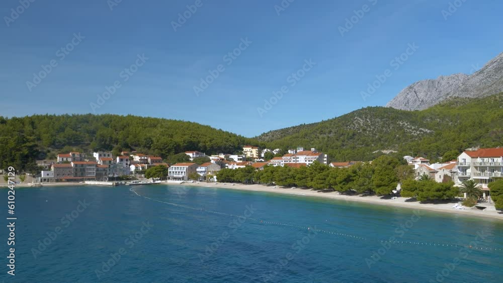 AERIAL: Beautiful empty beach and accommodation facilities outside tourist season. Peace and tranquillity in unoccupied tourist destination under rocky mountain range by the crystal blue Adriatic Sea. AERIAL: Beautiful empty beach and accommodation facilities outside tourist season. Peace and tranquillity in unoccupied tourist destination under rocky mountain range by the crystal blue Adriatic Sea.