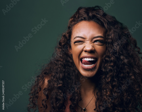 Natural beauty, tongue out and wink by gen z girl with hair, curly and fun on green background. Afro, hair care and female model flirt, emoji and silly face, personality or youth aesthetic in studio