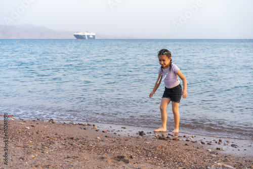 Cute little child playing on the beach. Little beautiful girl with braided hair walking barefoot on the seashore. © Inna