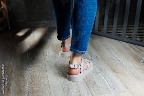 Beautiful slender female legs in leather sandals on the floor against gray parquet. Collection of women's sandals