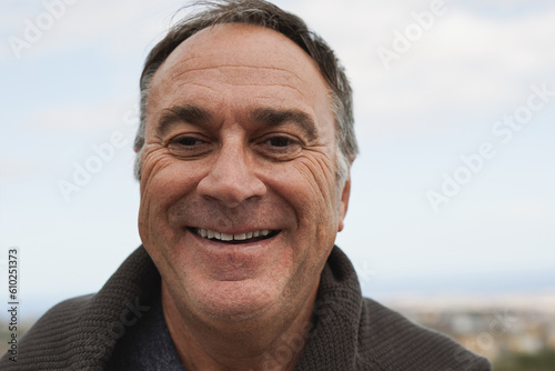 Happy senior man smiling on camera at house rooftop with ocean view in the background