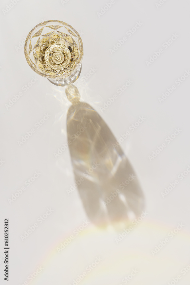 White wine in crystal transparent fashion glass with shadow and glare at sunlight, light white gray background, creative summer rest alcohol drink minimal concept, copy space, top view