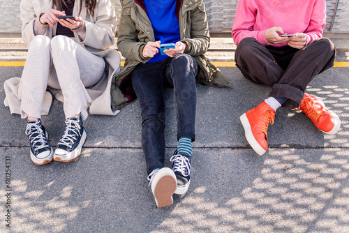 three unrecognizable friends sitting in the floor scrolling together through social media with mobile phone, concept of friendship and modern lifestyle