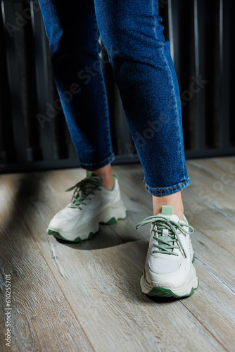 White leather summer sneakers on female legs in jeans. Women's casual sneakers. Comfortable women's shoes