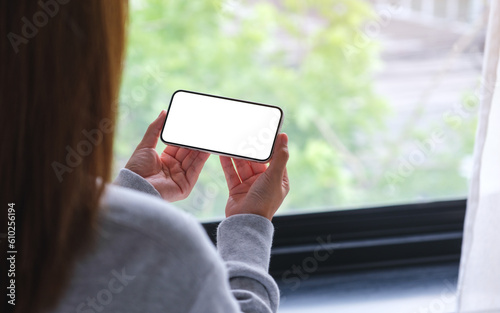 Mockup image of a woman holding and using mobile phone with blank desktop white screen at home
