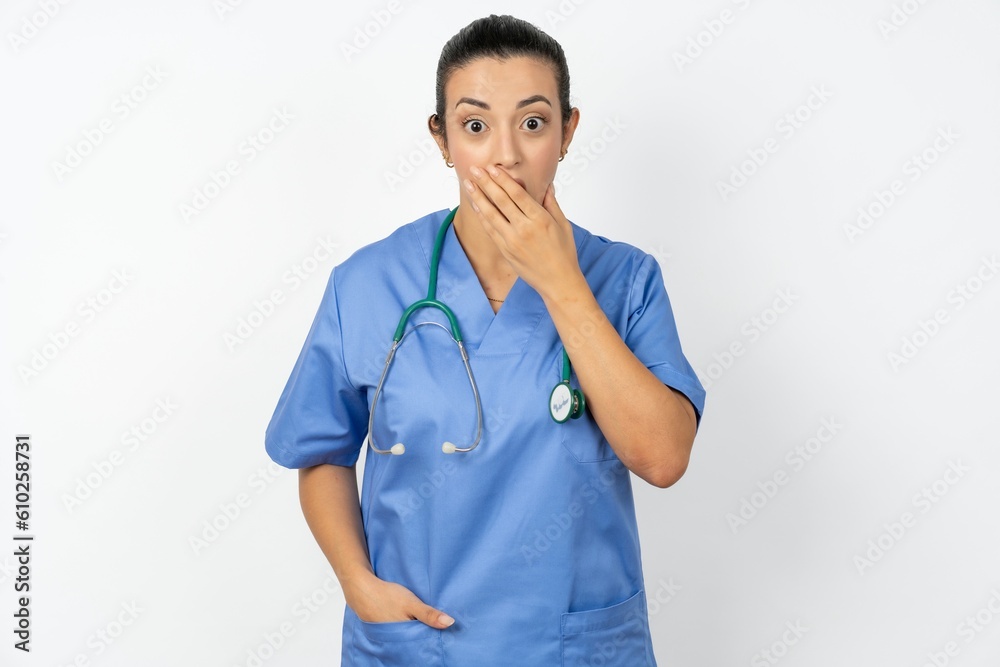 Emotional Beautiful doctor woman standing over white studio background gasps from astonishment, covers opened mouth with palm, looks shocked at camera. Emotional Beautiful doctor woman standing over white studio background gasps from astonishment, covers opened mouth with palm, looks shocked at camera.