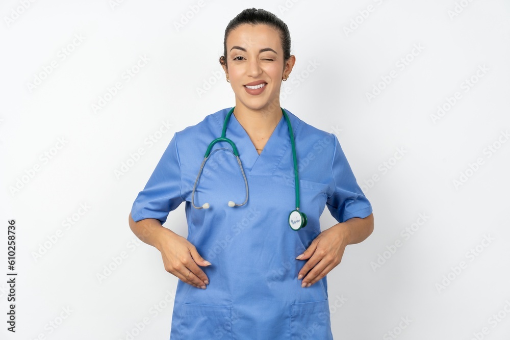 Coquettish Beautiful doctor woman standing over white studio background smiling happily, blinking at camera in a playful manner, flirting with you. Coquettish Beautiful doctor woman standing over white studio background smiling happily, blinking at camera in a playful manner, flirting with you.