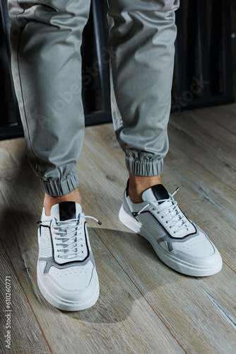 Male legs in white leather summer shoes. Comfortable men's white sneakers with laces. Casual men's sneakers