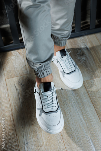 Casual white sneakers for men. Male legs in white leather summer shoes. Comfortable men's white sneakers with laces.