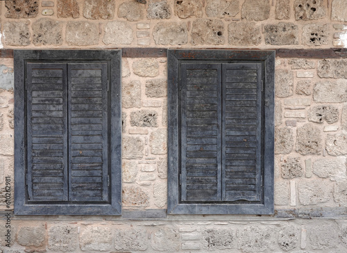 Vintage ancient wall from old sandy limestone and two closed windows with wooden shutters front view close-up