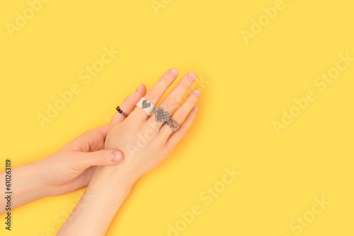 Female hands with multicolored rings made of beads on a yellow background. Fashion concept with place for text.