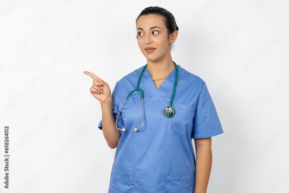 Beautiful doctor woman standing over white studio background points at copy space and advertises something, advices best price. Beautiful doctor woman standing over white studio background points at copy space and advertises something, advices best price.