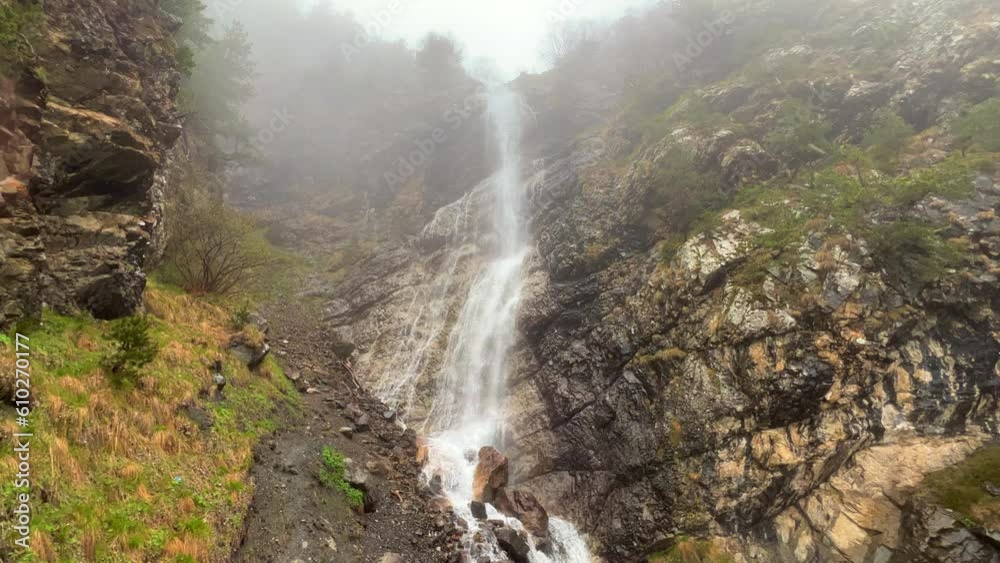 Hares waterfall in rainy weather in the mountains. A thick fog is spreading over the pine forest. Shooting a waterfall in spruce forests on mountain hills on a foggy day. North Ossetia. Digoria Gorge.