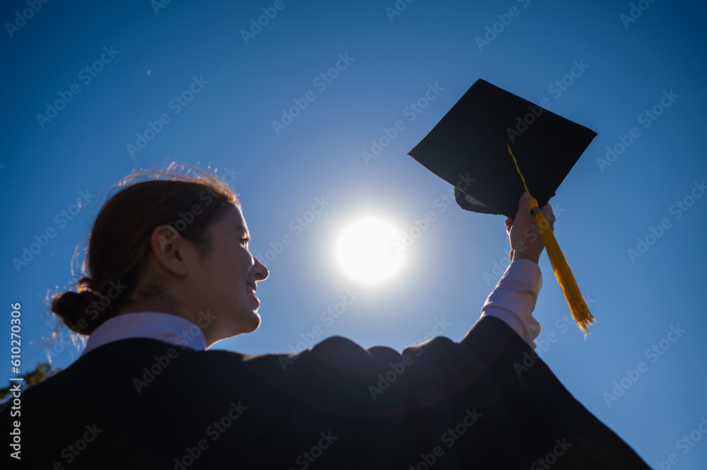 A woman throws her graduation cap against the blue sky. - obrazy, fototapety, plakaty 