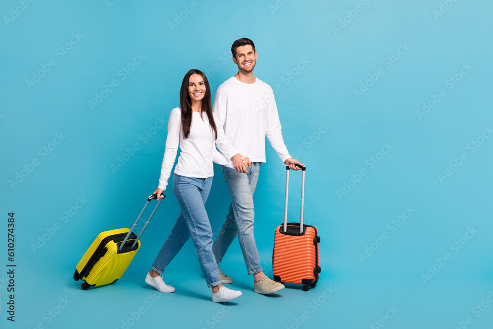Full size photo of two cheerful positive satisfied persons wear white shirts go to the gate in airport isolated on blue color background Full size photo of two cheerful positive satisfied persons wear white shirts go to the gate in airport isolated on blue color background