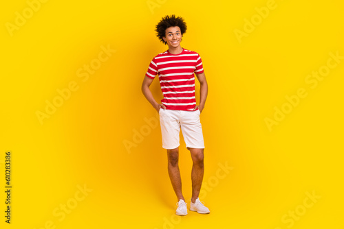 Full length photo of cool cheerful man wear striped t-shirt smiling walking isolated yellow color background © deagreez