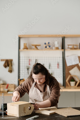 Vertical image of girl with down syndrome in protective glasses making birdhouse in workshop © AnnaStills