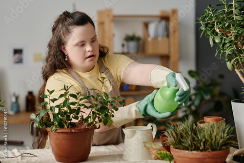 Girl with down syndrome watering green plants with sprayer while ransplanting them in pots photo