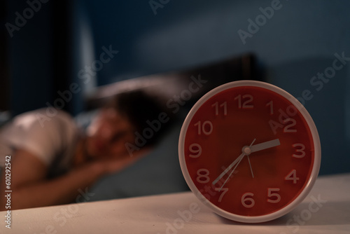 Depressed tired young man lying in bed at night cannot sleep from insomnia. Focus on clock. Insomnia