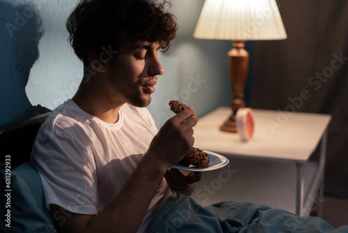 Stressed young man having a cookies at night. Unhappy tired depressed person eating during nighttime. Insomnia photo