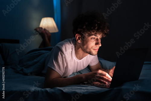 Fotografiet Young internet addict man networking concentrated late at night on bed with lapt
