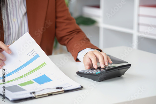 businesswoman working in the office Using calculator to calculate financial reports. Sales data with laptop computer and business documents on office table. Close up. Business finance and investment.