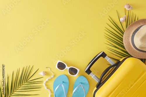 Dive headfirst into the spirit of a summer adventure! Top view flat lay of yellow travel case, seaside essentials, tropical leaves, seashells on yellow background with empty space for text or ad photo