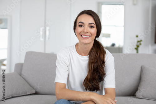 Beautiful positive woman sitting on the couch looking at the camera, online communication.