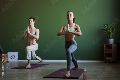 Full length portrait of smiling young woman as yoga instructor doing stretches indoors, copy space