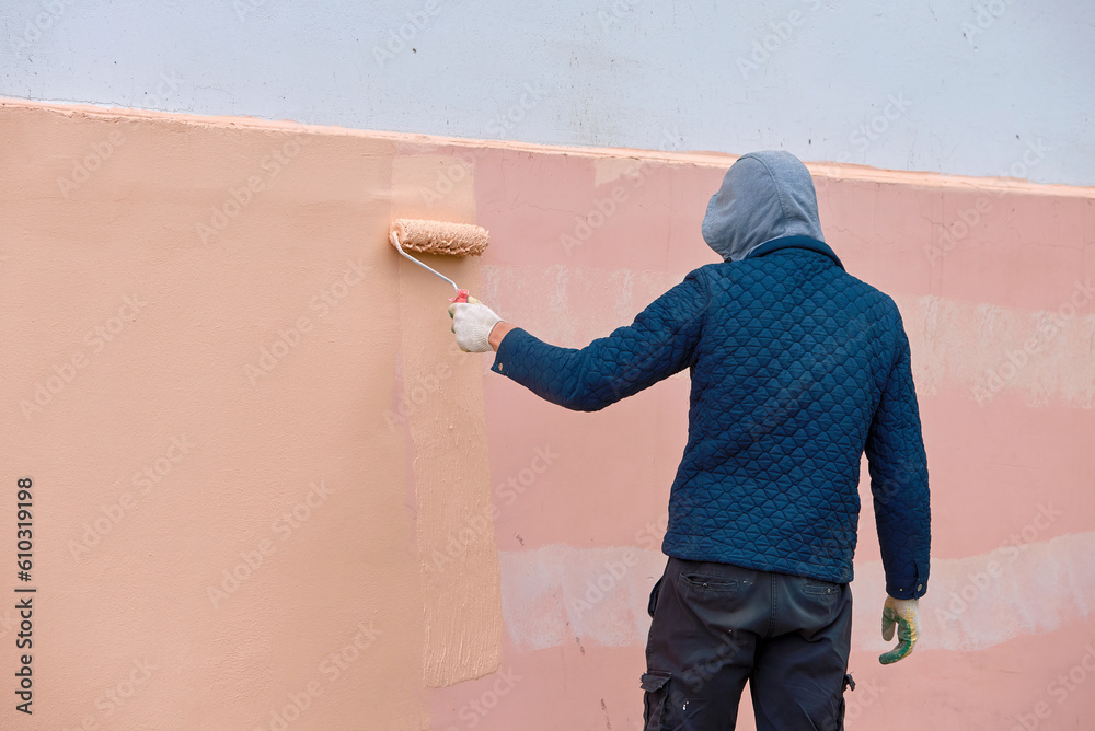 Man remove graffiti from building, painting wall with paint roller