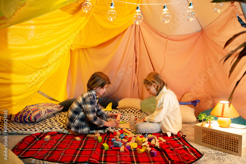 Two boys one brunette and the other blond are playing with airplanes inside a big blanket fort