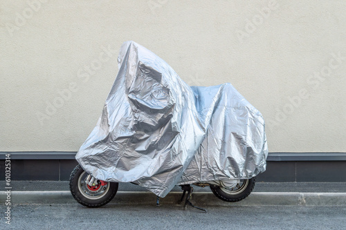 The motorcycle is covered with a silver cover against the wall