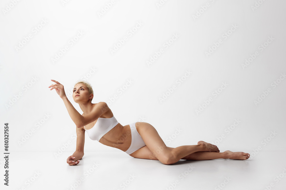 Tenderness. Portrait of young attractive woman with slim, fit body shape posing in underwear against grey studio background