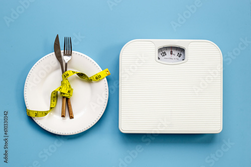 Weight scale and tape measure over dinner fork and knife on the plate