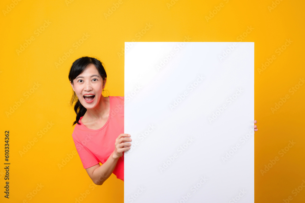 young asian sports fitness woman happy smile wearing pink sportswear standing behind the white blank banner or empty space advertisement board against yellow background. wellbeing lifestyle concept. young asian sports fitness woman happy smile wearing pink sportswear standing behind the white blank banner or empty space advertisement board against yellow background. wellbeing lifestyle concept.