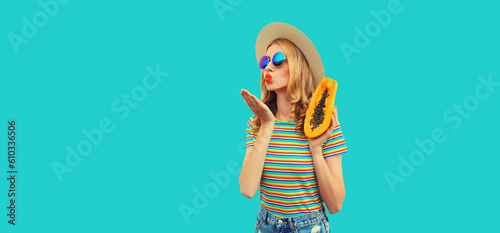 Summer portrait of young woman model posing with fresh papaya fruits wearing straw hat, sunglasses on blue background