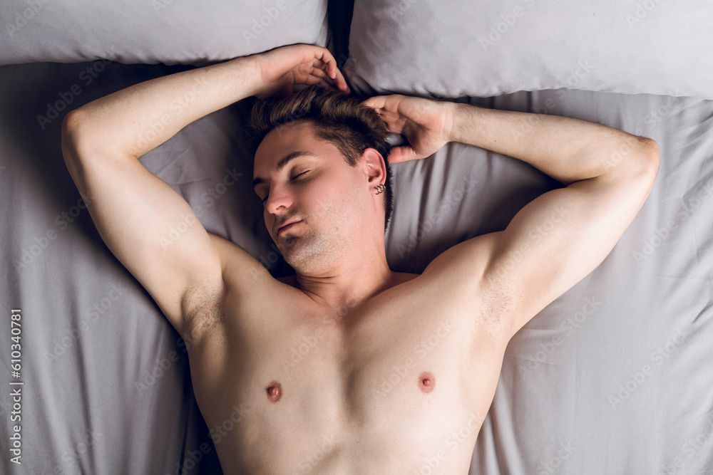 Handsome slim young man shirtless in the bed, sleeping with arms up