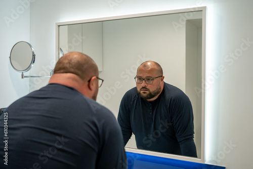 Sad fat lonely man looks in mirror bath, thinks change life, problems with self-acceptance. Depressed male has midlife crisis, health problems due obesity, no friends, mental disorders. Loneliness photo