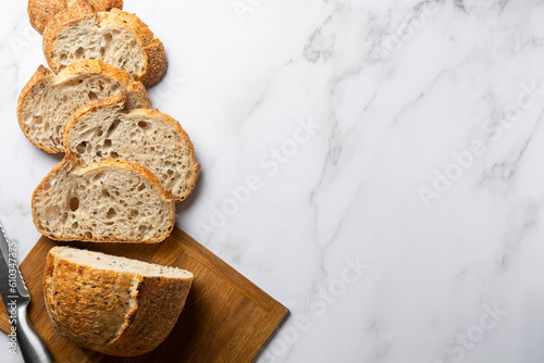 Sourdough Wheat Bread sliced on a wooden cutting board with a knife. Healthy natural bread made from organic products. Copy space banner on marble white background. Top view.