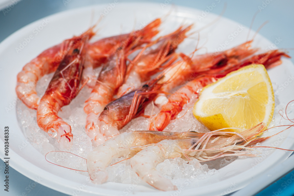 Plate of raw fresh red prawns and shrimps ready to eat with a slice of lemon and ice in a fish market in Bari, Puglia, Italy Plate of raw fresh red prawns and shrimps ready to eat with a slice of lemon and ice in a fish market in Bari, Puglia, Italy