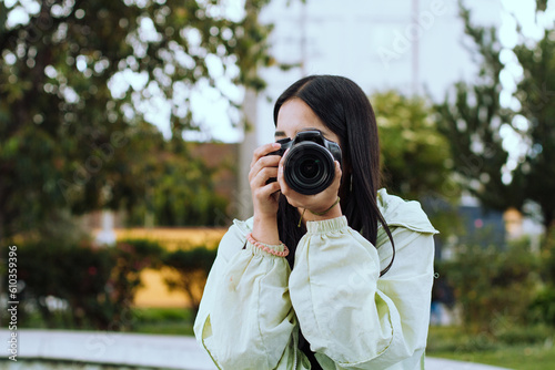 Photograph of a young woman in her 20's taking pictures with a professional camera on a sunny afternoon in a park in South America.