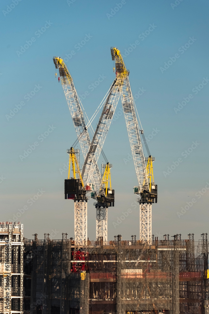 Huge double cranes on a building in construction, at sunset
