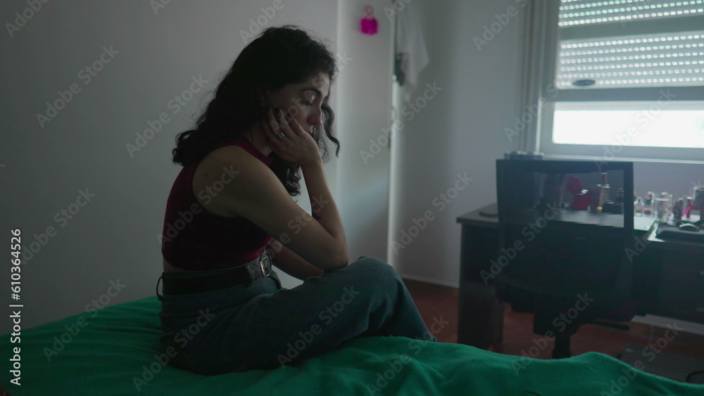 One pensive preoccupied young woman sits by bedside with contemplative expression. Female person in 30s struggling with inner emotions
